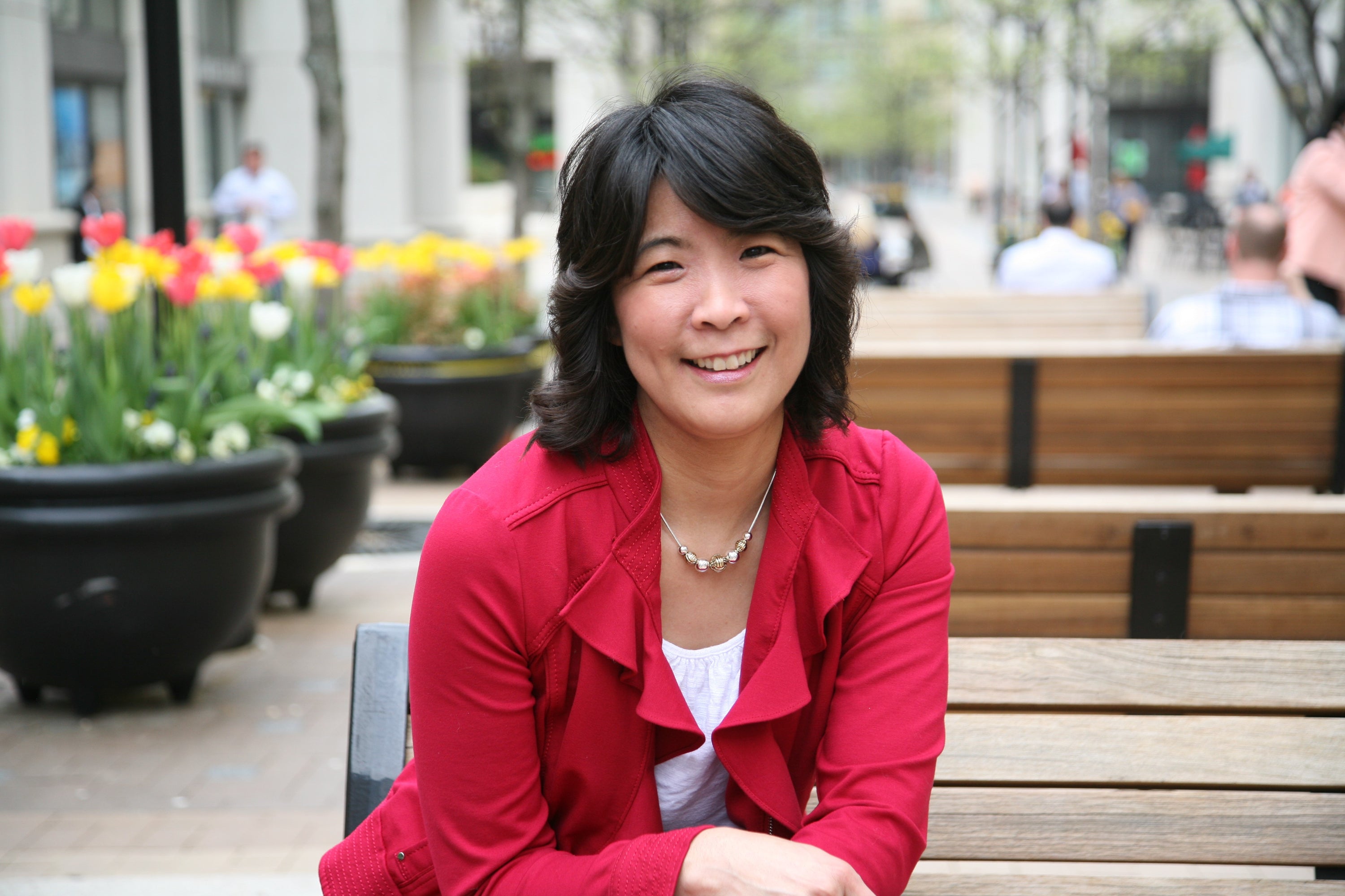 Asian-American founder in a casual white shirt and red, ruffled jacket. Seen smiling, celebrating that she found her passion..