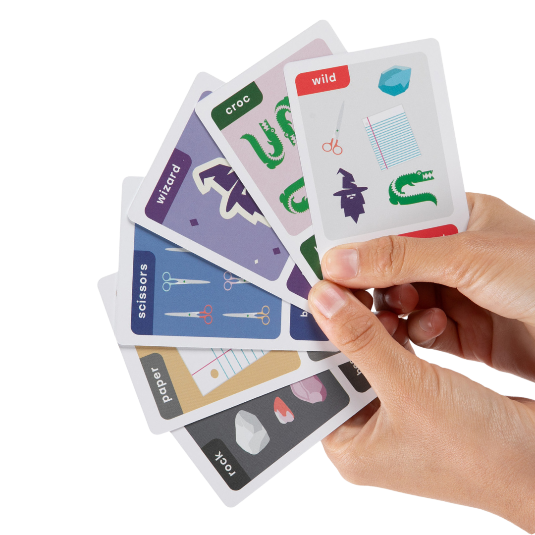 Close-up of hand holding one of each Rock, Paper, Scissors, Wizard, Crocodile, and Wild card. Imagery is colorful and playful..