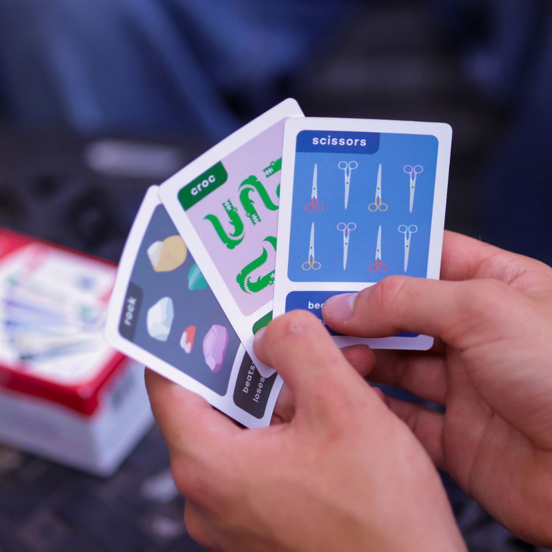 Close-up view of an RPSWC player's hands holding Rock, Croc, and Scissors cards.