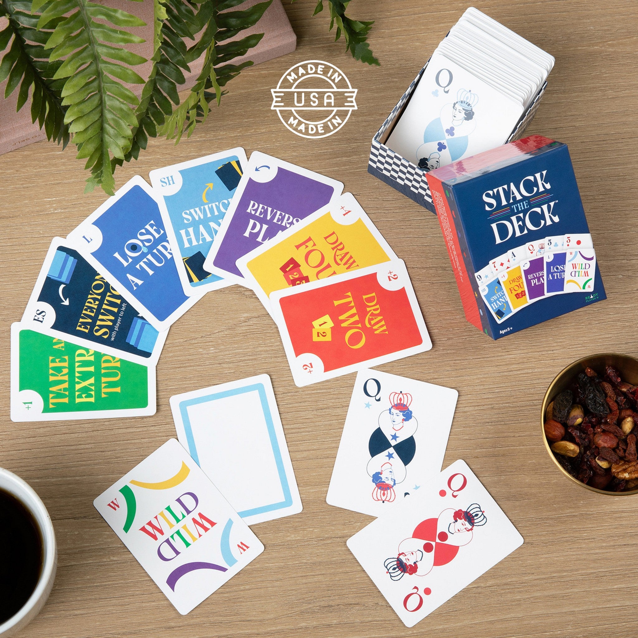 Playing cards with colorful text on a wooden table with a cup of coffee and a bowl of snacks.